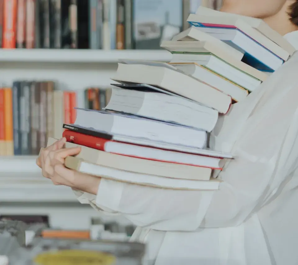 Une personne portant une pile de livres dans une bibliothèque