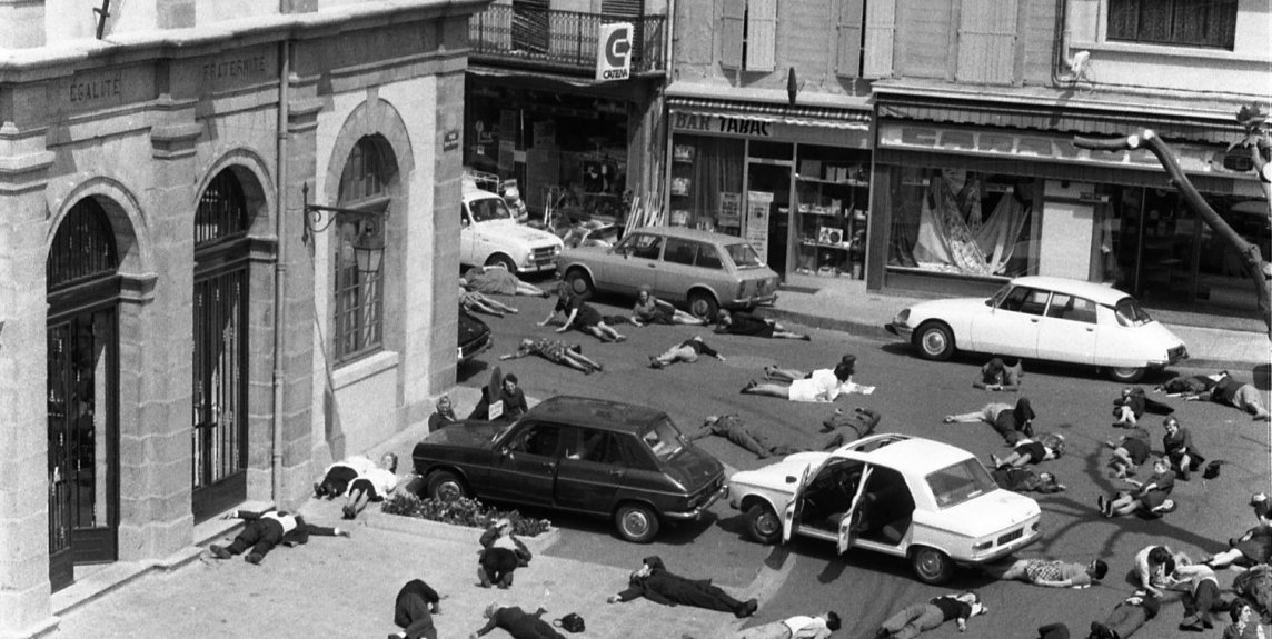 Photo : Vue d'ensemble en plongée d'un grand nombre de personnes couchées au milieu de la rue et sur les trottoirs (comme si elles étaient mortes), voitures arrêtées portières ouvertes, 1973. Cliché pris lors de l'opération médiatique "Mazamet ville morte" organisée par la Sécurité routière.