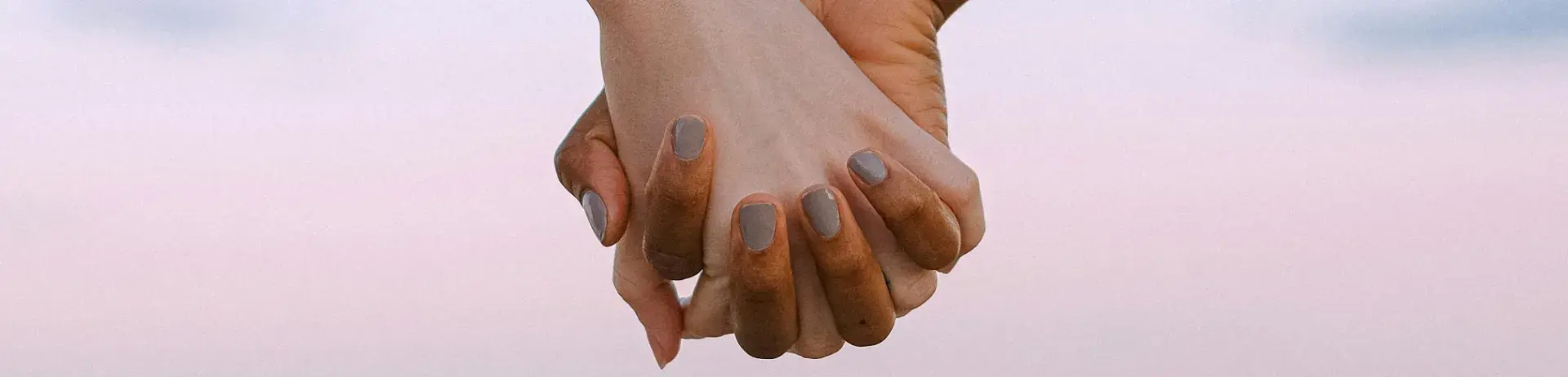 Deux mains enlacées, l'une noire, l'une blanche, sur fond de ciel rosé